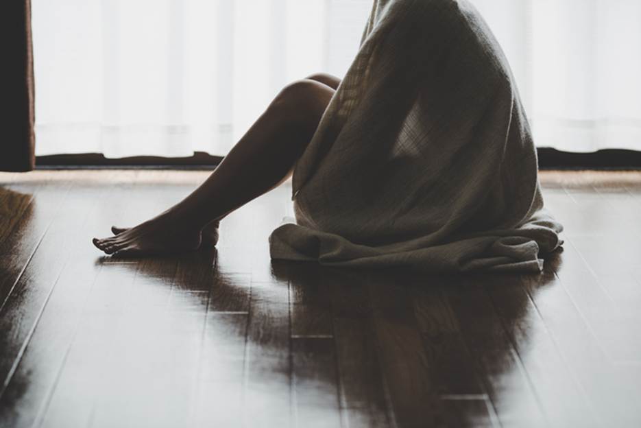 A figure sits on a wood floor, covered in a blanket, in front of a window. The image relates to content about workplace harassment and employee protections.